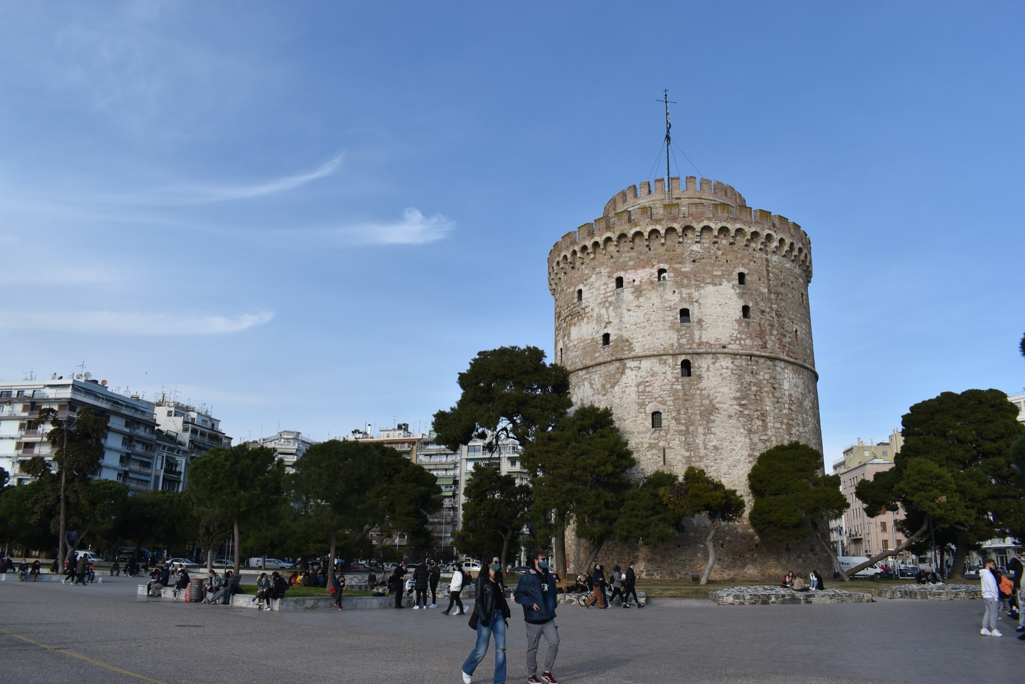 The White Tower of Thessaloniki under a blue sky, with people strolling the waterfront promenade