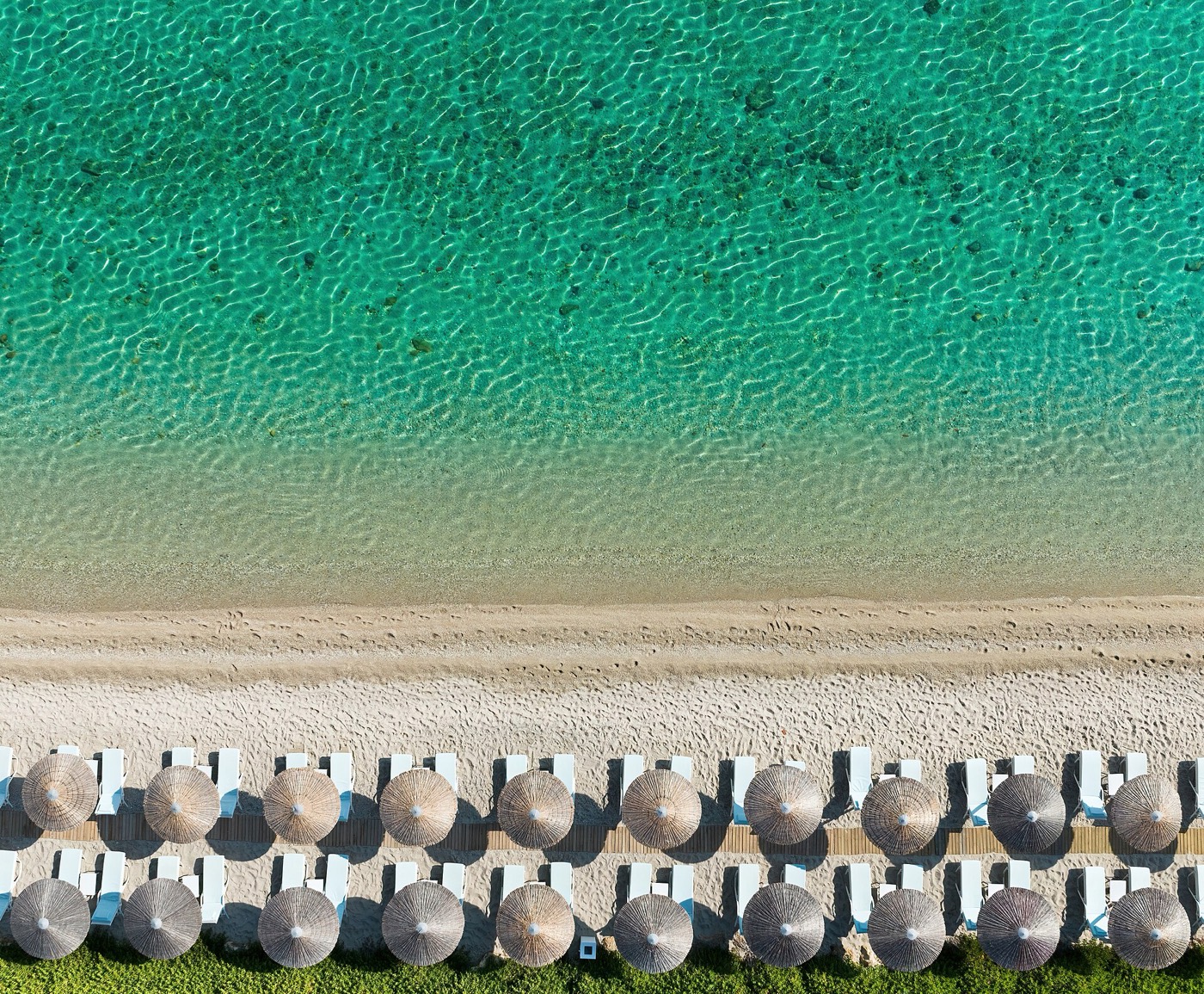 Aerial view of straw umbrellas on a sandy beach with turquoise water on Kassandra